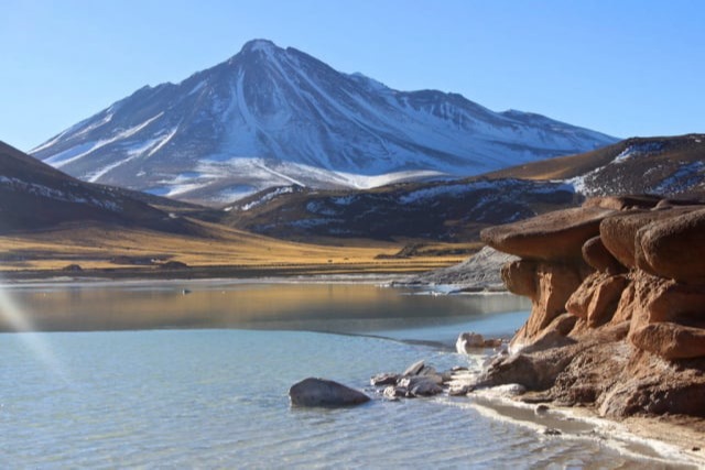 Red rocks on the shore of the salt flat with a snow-capped volcano at Piedras Rojas